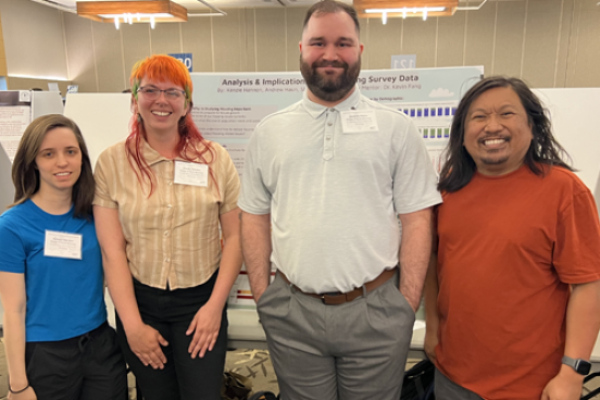 Three students and Dr. Fang standing in front of poster in research colloquium