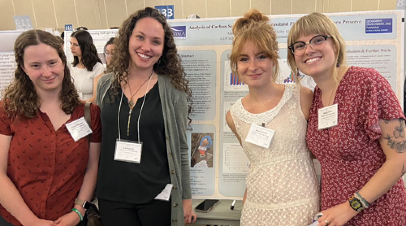 Four students standing in front of poster in research colloquium