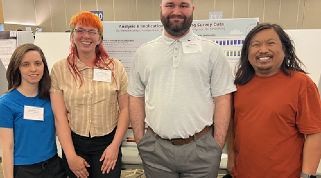 Three students and Dr. Fang standing in front of poster in research colloquium